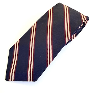 May include: A navy blue necktie featuring a repeating pattern of diagonal stripes. Each stripe consists of a thin, cream-colored line flanked by two narrow burgundy lines, creating a structured and classic appearance across the fabric surface.