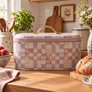 May include: An oval metal bread bin featuring a hand-painted pink, white, and yellow chequered pattern. The container has a removable lid with a gold-toned arched handle and a gold-toned rim around the base, providing a secure storage solution.