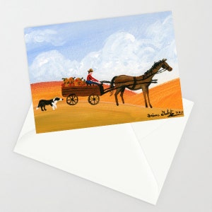 May include: A greeting card featuring a painting of a horse-drawn wagon filled with pumpkins, driven by a person in a red shirt and hat. A black and white dog walks alongside the wagon. The background shows a blue sky and a field.