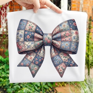 Pode incluir: Uma sacola branca com um grande design de laço. O laço é composto por quadrados de patchwork em tons de azul, rosa e verde, adornados com padrões florais. O centro do laço apresenta rosas cor-de-rosa.