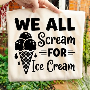 Puede incluir: Una bolsa de mano de color crema con la frase "WE ALL Scream FOR Ice Cream" en letras negras en negrita. También presenta un gráfico de cono de helado negro con tres bolas y detalles de goteo. La bolsa está sostenida por una mano.