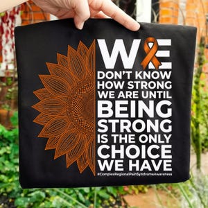 May include: Black t-shirt with an orange sunflower design and the text "WE DON'T KNOW HOW STRONG WE ARE UNTIL BEING STRONG IS THE ONLY CHOICE WE HAVE". An orange ribbon is also featured. The hashtag is #ComplexRegionalPainSyndromeAwareness.