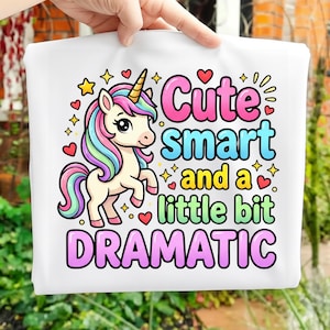 Puede incluir: Bolso tote blanco con una ilustración de unicornio colorido. El texto "Cute, Smart, and a little bit Dramatic" está escrito en rosa, azul y verde, con estrellas y corazones.