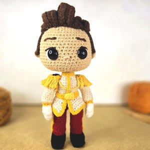 Peut inclure: Poupée au crochet faite à la main représentant un homme en uniforme de style militaire. La poupée a un visage bronzé, des cheveux bruns et des yeux noirs. L'uniforme est blanc avec des détails dorés, un pantalon rouge et des bottes noires.
