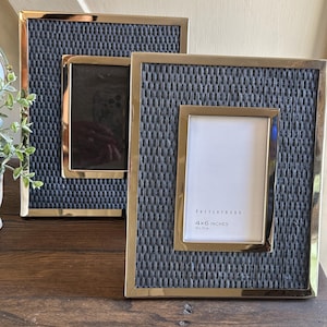 May include: Three rectangular photo frames with gold-colored trim and a woven navy blue background. The frames are in different sizes, with one labeled "4x6 INCHES". The frames are displayed on a wooden surface.