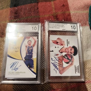 Puede incluir: Dos tarjetas de baloncesto de Victor Wembanyama calificadas, en protectores de plástico transparente. Ambas tarjetas tienen una calificación de 10. Una tarjeta está etiquetada como "Draft 2023", la otra como "2023 Autograph Express Promo Rookie".
