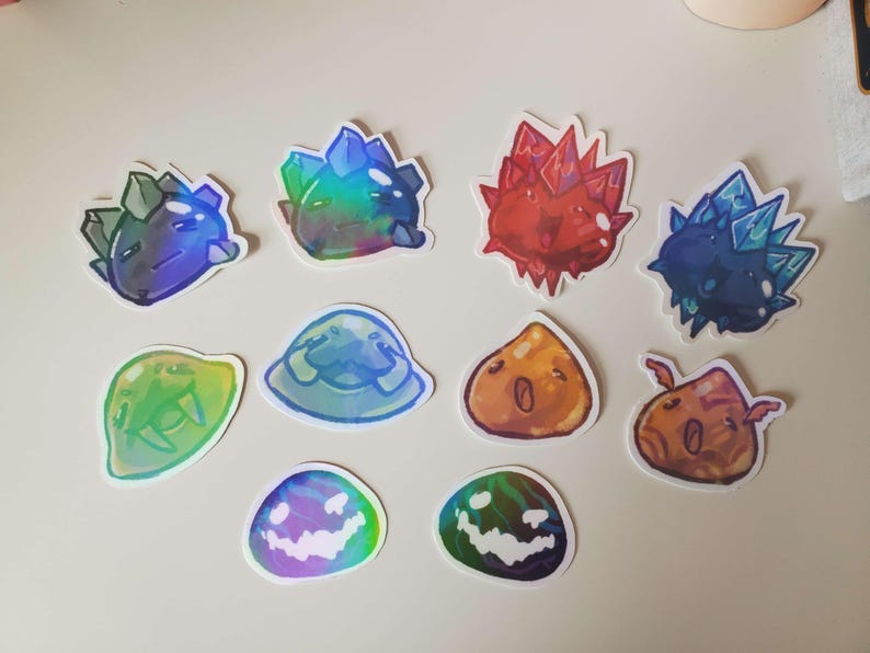 May include: A collection of colorful, cartoonish stickers featuring various crystal and slime designs. The stickers showcase a range of colors, including blue, green, red, and orange, with some having a holographic effect. The designs include spiky crystals and blob-like slimes.