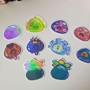 May include: A collection of colorful, die-cut stickers featuring various cartoon slime characters. The stickers showcase a range of colors, including blue, green, purple, and red, with some designs incorporating crowns and other details. These stickers are ideal for decorating notebooks, laptops, or other items.