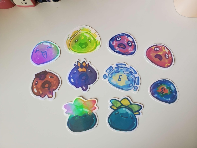 May include: A collection of colorful, die-cut stickers featuring various cartoon slime characters. The stickers showcase a range of colors, including blue, green, purple, and red, with some designs incorporating crowns and other details. These stickers are ideal for decorating notebooks, laptops, or other items.