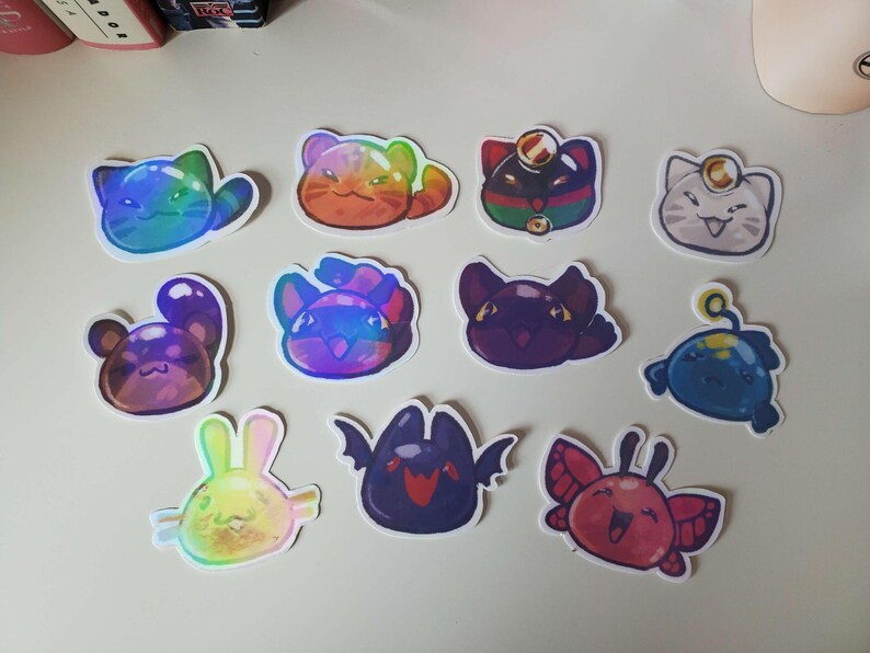 May include: A collection of colorful, holographic stickers featuring various cartoon creatures. Designs include cats, bunnies, and other whimsical characters in shades of blue, purple, orange, and red. Each sticker has a white border.