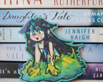 May include: A colorful sticker featuring a cartoon character with long, dark hair and a frog-like appearance. The character is depicted with a light skin tone, green eyes, and a smiling expression. The sticker is surrounded by a green and blue border, and is placed in front of a stack of books.