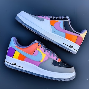 May include: Two colorful Air Force 1 sneakers. The shoes feature a white sole, gray and black accents, and a vibrant mix of orange, purple, blue, and yellow panels. The word "AIR" is printed in black on the side of the white sole.