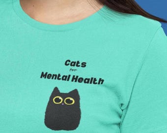 May include: Teal t-shirt with the text "Cats for Mental Health" above a black cat illustration with yellow eyes. The shirt is made of a soft material and has short sleeves.