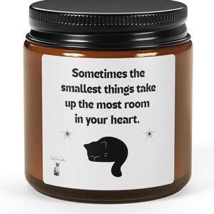 May include: A brown candle jar with a black lid and a white label. The label features the text "Sometimes the smallest things take up the most room in your heart." A black cat silhouette is also on the label.