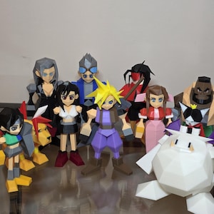 Puede incluir: Una colección de figuras de papel de personajes de Final Fantasy VII. Las figuras son de varios colores, incluyendo azul, amarillo, negro, rojo y morado. Las figuras están sobre una superficie reflectante.