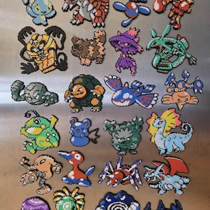 May include: A collection of twenty-four pixel art figures crafted from colorful plastic fuse beads. The assortment features various creature designs in diverse shapes and vibrant colors, including shades of blue, red, green, orange, and purple, arranged in a grid pattern.