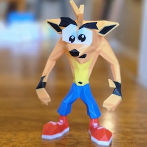 May include: A low-poly figurine of a character with orange skin, large white eyes with black pupils, and black eyebrows. The figure wears a yellow chest patch, blue trousers, black wrist cuffs, and red shoes with white soles, featuring a spiky orange hair tuft.
