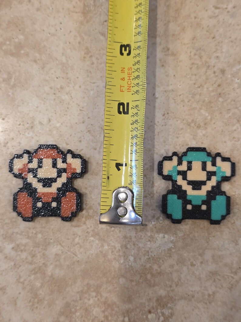 Puede incluir: Dos figuras de pixel art, una roja y otra turquesa, junto a una cinta m&eacute;trica. Las figuras miden aproximadamente 2,5 cm de alto. Las figuras est&aacute;n hechas de peque&ntilde;as cuentas de colores.