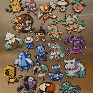 May include: A collection of twenty-two pixel art figures crafted from colorful plastic beads. The assortment features various stylized creatures in shades of blue, orange, purple, green, and white, each displaying distinct shapes and character designs.