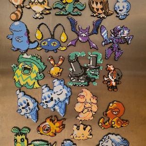 May include: A collection of colorful pixel art magnets featuring various cartoon characters. The magnets showcase a variety of creatures in shades of blue, orange, yellow, green, and purple. The collection includes a diverse range of designs.