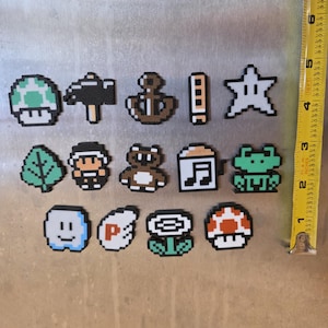 Puede incluir: Colecci&oacute;n de imanes pixelados con varios dise&ntilde;os. Incluye un hongo verde, martillo, ancla, estrella, hoja, personaje, oso, nota musical, rana, cara sonriente, s&iacute;mbolo P, flor y hongo rojo. La cinta m&eacute;trica muestra una longitud de aproximadamente 15 cm.