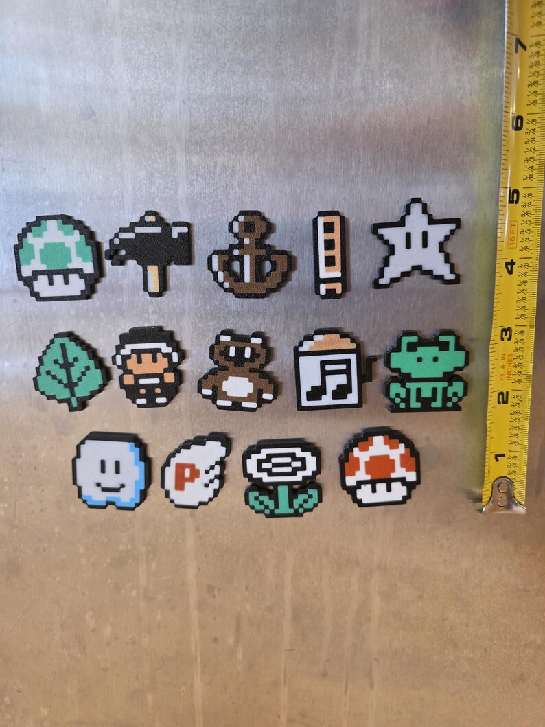 Puede incluir: Colecci&oacute;n de imanes pixelados con varios dise&ntilde;os. Incluye un hongo verde, martillo, ancla, estrella, hoja, personaje, oso, nota musical, rana, cara sonriente, s&iacute;mbolo P, flor y hongo rojo. La cinta m&eacute;trica muestra una longitud de aproximadamente 15 cm.