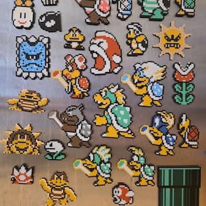 Puede incluir: Una colecci&oacute;n de imanes pixelados con personajes de la serie de videojuegos Super Mario. Los imanes incluyen a Mario, Bowser, Goombas y Koopa Troopas, en colores vibrantes. La colecci&oacute;n incluye una tuber&iacute;a verde.