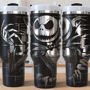 Könnte beinhalten: Schwarze Reisebecher mit weißem Deckel und Griff, mit einer silbernen Illustration von Jack Skellington aus The Nightmare Before Christmas. Das Design umfasst Skeletthände und Jacks Gesicht.