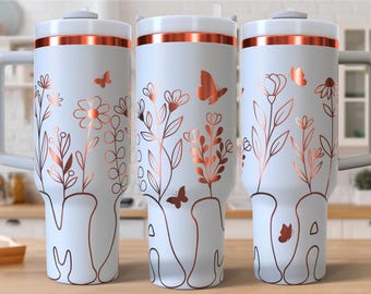 Puede incluir: Tres vasos aislados blancos con diseños florales y de mariposas en oro rosa. Cada vaso tiene un asa y una tapa con una banda de oro rosa. El diseño floral incluye flores, hojas y mariposas.