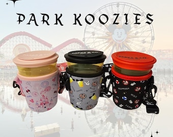 Könnte beinhalten: Drei isolierte Getränkehalter mit Deckeln und Trageriemen. Einer ist rosa mit einem Schlossdesign, einer ist grau mit Parksymbolen und der letzte ist schwarz mit dem Thema "Happiest Place on Earth". Der Text "PARK KOOZIES" steht oben.