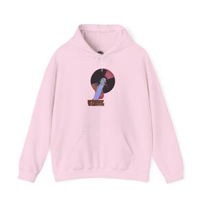 May include: A light pink hoodie with a front pocket and drawstring hood. The front features a graphic of a woman with a record and the word "VINYL" in brown block letters. The record has a rainbow color scheme.