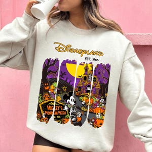 May include: A light gray Disneyland sweatshirt featuring a Halloween-themed graphic. The graphic includes Mickey Mouse, pumpkins, a haunted house, and the text "Mickey's Pumpkin Patch" and "Disneyland Est. 1955".