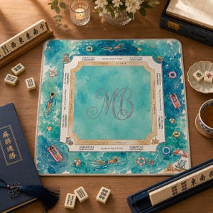 May include: A square mahjong mat featuring a watercolor pool scene with swimmers, floats, and beach items. The center has a light blue area with the monogram MB. The border includes game instructions and Charleston rules in black text.