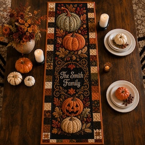Könnte beinhalten: Ein rechteckiger, gesteppter Tischläufer mit einem schwarzen Mittelteil, bedruckt mit Kürbissen, Herbstblättern und dem Text The Smith Family. Der Rand besteht aus einem Patchwork-Muster in den Farben Orange, Braun und Creme mit Steppnähten.