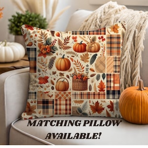May include: Square decorative pillow with a patchwork design featuring pumpkins, fall leaves, and plaid patterns in shades of orange, brown, and cream. The pillow is on a white couch with a matching pumpkin nearby. Text on the pillow reads "MATCHING PILLOW AVAILABLE!"