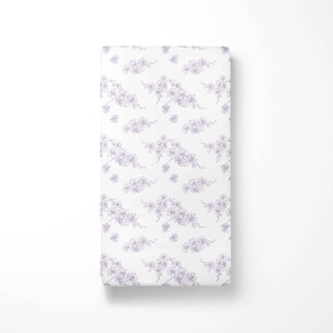 May include: White rectangular fabric featuring a repeating pattern of lavender floral branches. The branches have delicate leaves and small flower clusters. The fabric is folded neatly, suggesting it is a sheet or blanket.