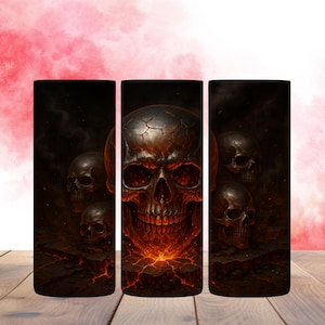 May include: A set of three tall, cylindrical tumblers featuring a detailed, fiery skull design. The central tumbler showcases a large, cracked skull with glowing orange and red accents, surrounded by smaller skulls against a dark, smoky background. The overall theme is gothic and macabre.