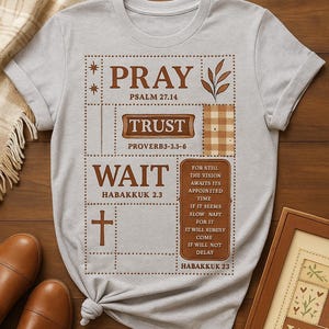 Könnte beinhalten: Hellgraues T-Shirt mit braunem Grafikdesign mit den Wörtern "PRAY", "TRUST" und "WAIT" sowie Bibelversen. Das T-Shirt ist unten geknotet. Braune Lederschuhe sind sichtbar.