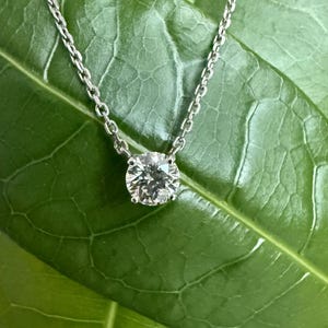 Peut inclure: Un collier &agrave; cha&icirc;ne en m&eacute;tal argent&eacute; avec un pendentif en pierre pr&eacute;cieuse transparente, ronde et facett&eacute;e, maintenu par un sertissage &agrave; quatre griffes. La cha&icirc;ne d&eacute;licate est reli&eacute;e au sommet de la pierre circulaire aux reflets multiples.