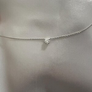 Peut inclure: Un collier &agrave; cha&icirc;ne fine de couleur argent&eacute;e orn&eacute; d'une unique petite pierre ronde transparente &agrave; facettes, fix&eacute;e au centre par un sertissage &agrave; griffes simple. La fine cha&icirc;ne m&eacute;tallique s'&eacute;tend horizontalement, pr&eacute;sentant un design &eacute;pur&eacute;.
