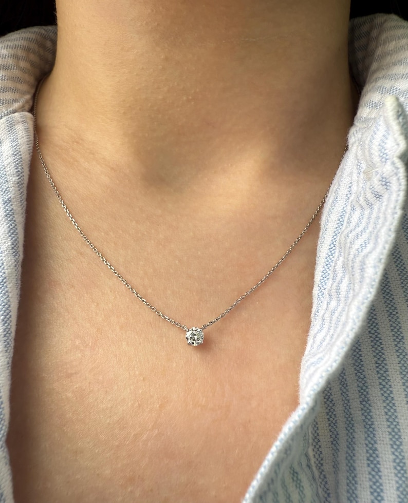 Peut inclure: Un collier &agrave; cha&icirc;ne fine de couleur argent&eacute;e orn&eacute; d'une unique petite pierre pr&eacute;cieuse transparente, ronde et taill&eacute;e en brillant, fix&eacute;e dans un sertissage m&eacute;tallique simple &agrave; quatre griffes. Le collier repose sur le cou avec une cha&icirc;ne fine.