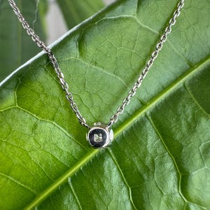 Peut inclure: Un collier &agrave; cha&icirc;ne en m&eacute;tal argent&eacute; dot&eacute; d'un petit pendentif en forme de cube. Le pendentif pr&eacute;sente une finition lisse et polie et contient une unique petite pierre claire de taille carr&eacute;e sertie en son centre, suspendu &agrave; une cha&icirc;ne fine.