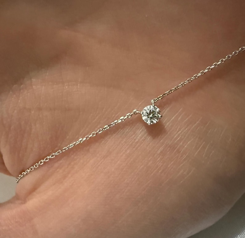 Peut inclure: Un collier &agrave; cha&icirc;ne fine de couleur argent&eacute;e orn&eacute; d'une unique petite pierre pr&eacute;cieuse transparente, ronde et taill&eacute;e en brillant, fix&eacute;e dans un serti &agrave; griffes simple. Le collier se compose de fins maillons circulaires entrelac&eacute;s.