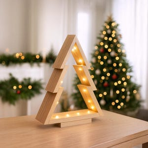 Könnte beinhalten: Weihnachtsbaumdekoration aus Holz mit warmweißen LED-Leuchten. Der Baum ist aus hellem Holz gefertigt und hat ein geometrisches Design. Der Baum steht auf einem Holztisch. Ein dekorierter Weihnachtsbaum ist im Hintergrund.