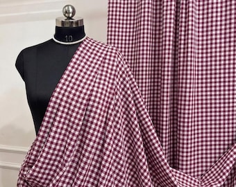 May include: A maroon and white gingham fabric draped over a black mannequin torso. The fabric features a consistent small-scale checkered pattern throughout. The mannequin displays the number 10 on its neck and wears a white beaded necklace.