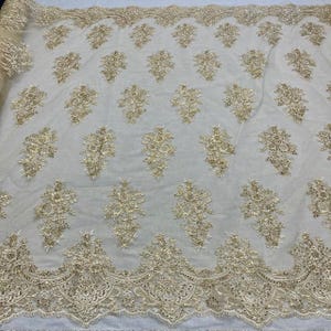 May include: Ivory-colored lace fabric with intricate gold floral embroidery. The fabric features a repeating pattern of detailed floral clusters and a scalloped edge. This elegant lace is suitable for bridal wear, evening gowns, or decorative projects.