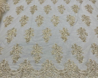 May include: Ivory-colored lace fabric with intricate gold floral embroidery. The fabric features a repeating pattern of detailed floral clusters and a scalloped edge. This elegant lace is suitable for bridal wear, evening gowns, or decorative projects.