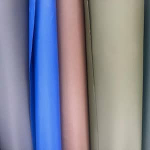 May include: Close-up of several rolls of fabric in various colors. The colors include shades of gray, blue, pink, and green. The fabric appears to be smooth and possibly synthetic.