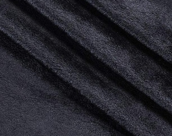 May include: Close-up of a dark navy blue plush fabric with a soft, textured surface. The fabric has a subtle sheen and is draped in diagonal folds, creating shadows and highlights.