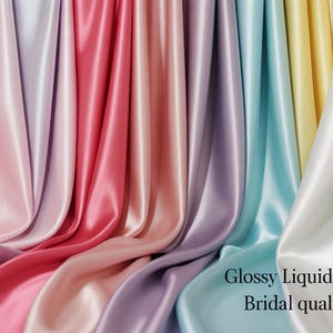 May include: A display of glossy liquid satin fabric in various pastel colours, including pink, red, purple, blue, and yellow. The fabric is 147 cm wide and of bridal quality. The fabric drapes in soft folds.